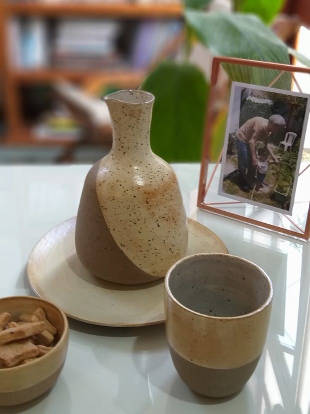 Um dos presentes perfeitos para o Dia dos Pais: moringa e copo de cerâmica, em tons de bege. Do lado direito, vemos um porta-retrato. Do lado esquerdo, uma tigela com biscoitos. 