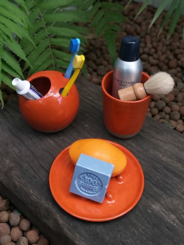 Copo, saboneteira e porta-escovas de dente em cerâmica laranja. 